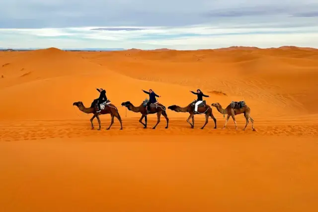 Fila de viajeros en dromedario atravesando las dunas de Erg Chebbi, en Merzouga, con luz de atardecer